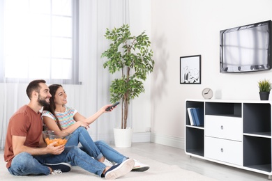Photo of Young couple sitting on floor and watching TV at home