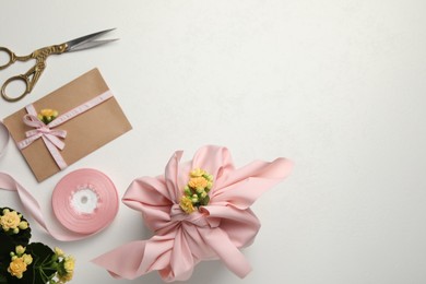Photo of Furoshiki technique. Gift packed in pink fabric, card, flowers and scissors on white table, flat lay. Space for text
