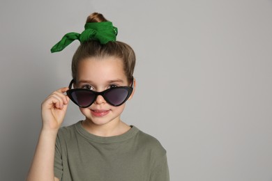 Photo of Cute little girl with stylish bandana and sunglasses on grey background, space for text
