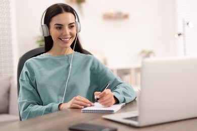 Photo of Young woman in headphones watching webinar at table in room