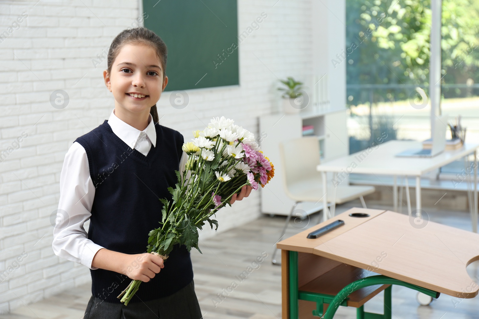 Photo of Happy schoolgirl with bouquet in classroom. Teacher's day