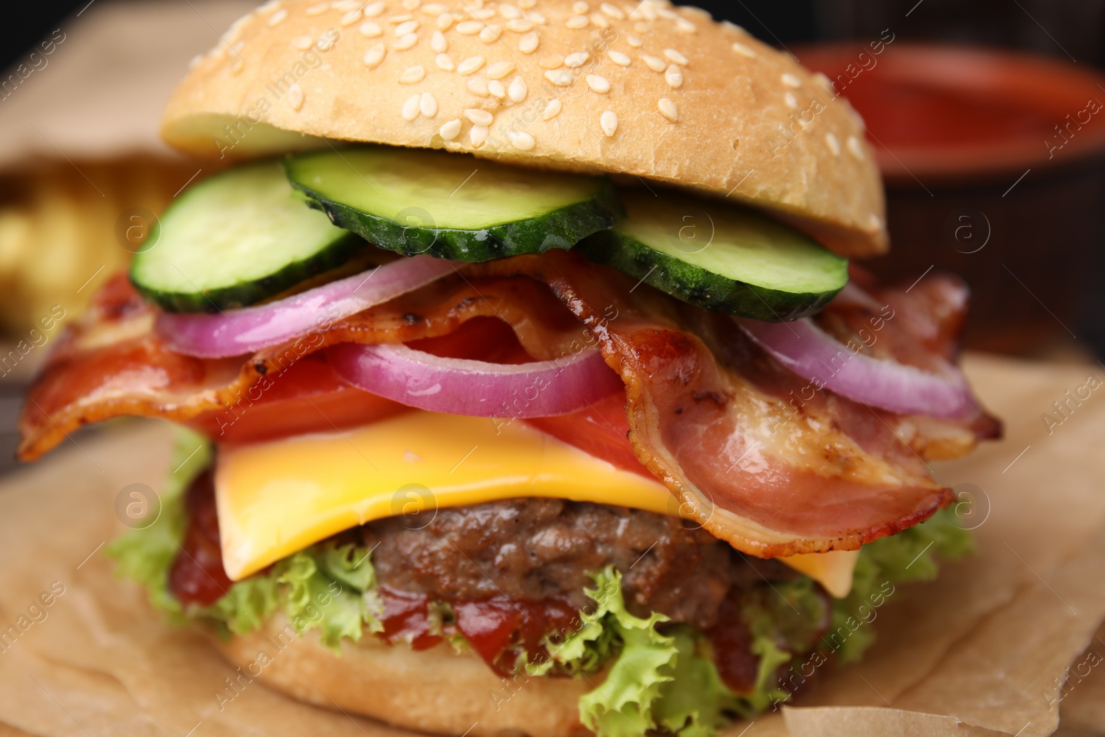 Photo of Tasty burger with bacon, vegetables and patty on parchment paper, closeup