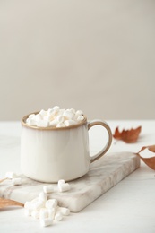 Cup of hot cozy drink with marshmallows and autumn leaves on table