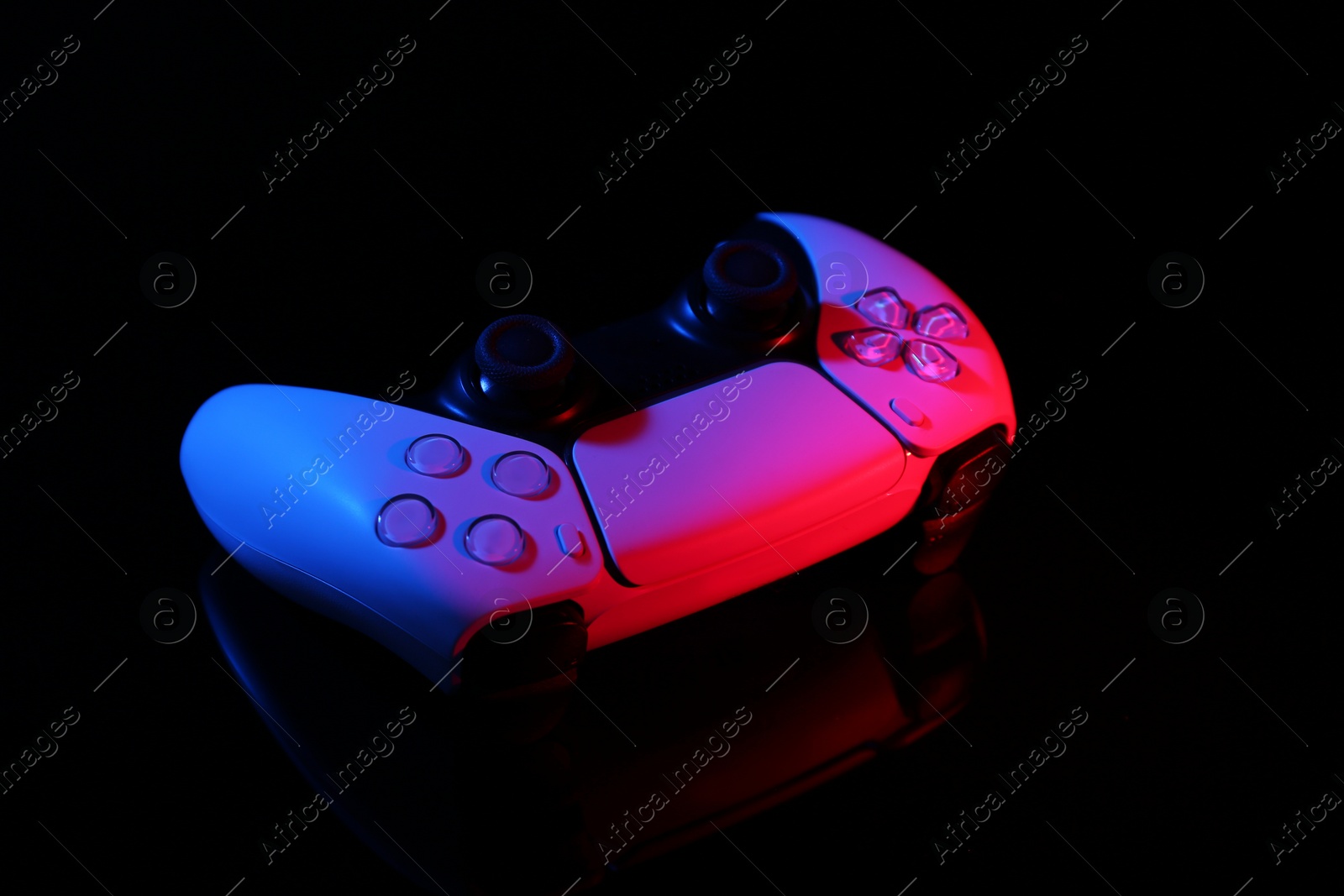 Photo of Wireless game controller on black mirror surface in neon lights