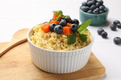 Photo of Tasty millet porridge with blueberries, pumpkin and mint in bowl on white table, closeup