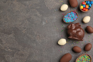 Flat lay composition with chocolate Easter bunny, eggs and candies on grey table. Space for text