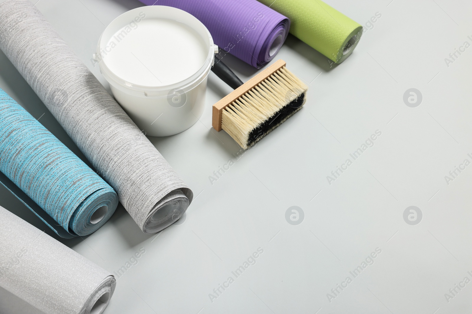 Photo of Different wallpaper rolls, brush and bucket with glue on light grey background, above view. Space for text