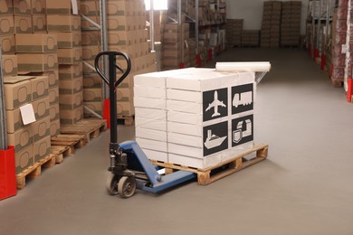 Image of Manual pallet truck with stacked boxes with shipping icons and roll of stretch wrap in warehouse