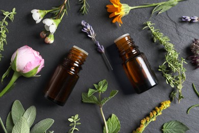 Photo of Bottles of essential oils, different herbs and flowers on black table, flat lay