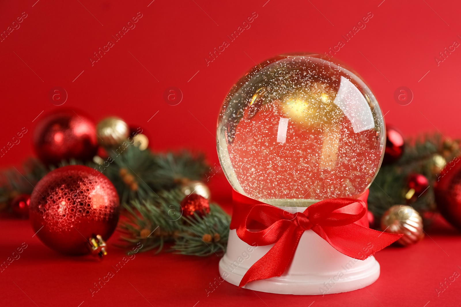 Photo of Beautiful snow globe, Christmas balls and fir branches on red background