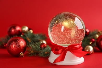 Beautiful snow globe, Christmas balls and fir branches on red background