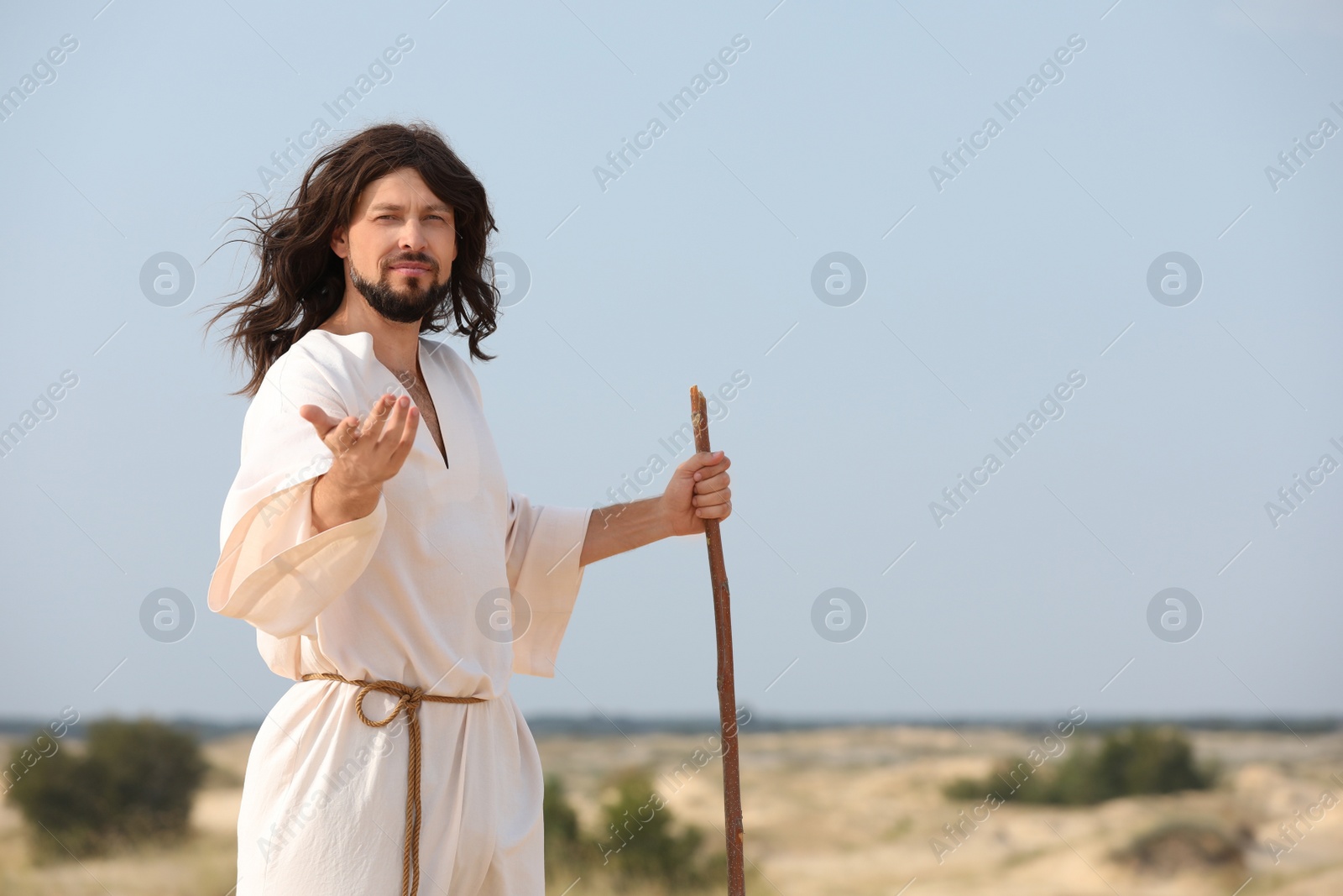 Photo of Jesus Christ walking with stick in desert. Space for text