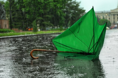 Broken green umbrella in park on rainy day