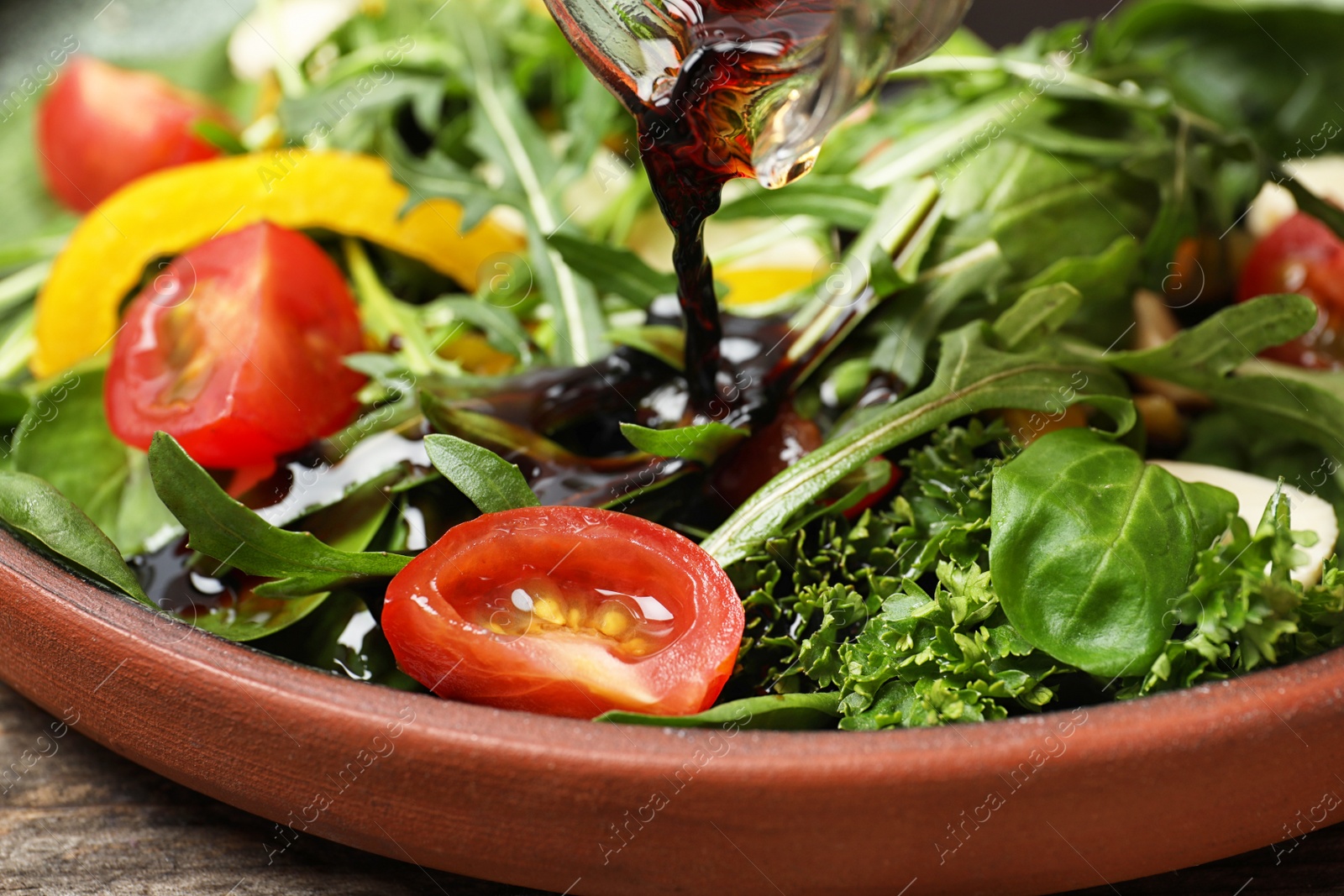 Photo of Pouring balsamic vinegar to fresh vegetable salad on plate, closeup