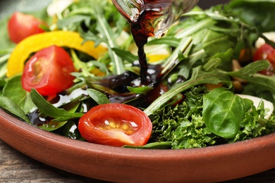 Pouring balsamic vinegar to fresh vegetable salad on plate, closeup