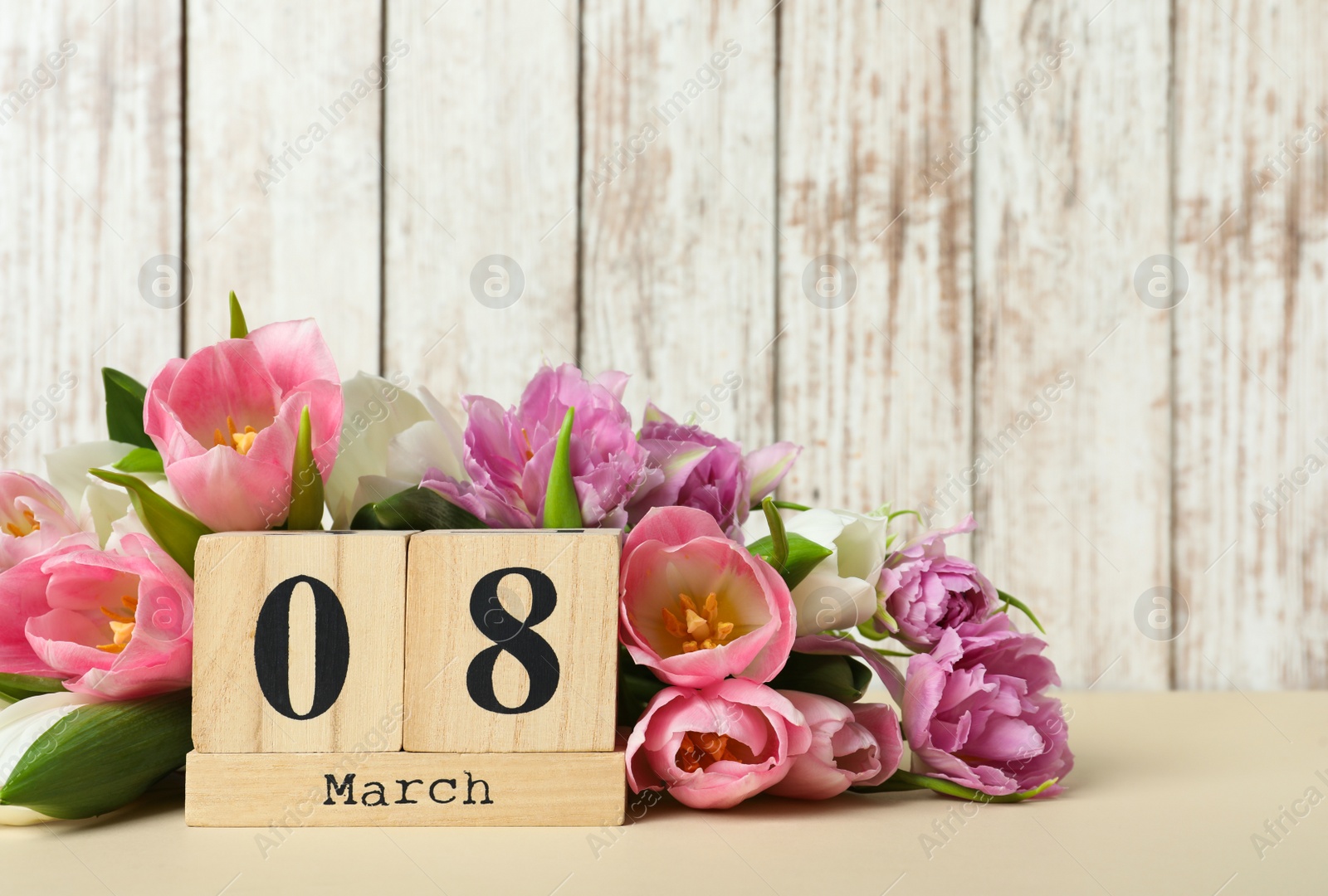 Photo of Block calendar with date 8th of March and tulips on table against wooden background, space for text. International Women's Day