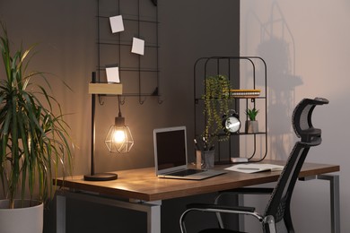 Photo of Cozy workplace with modern laptop on desk and comfortable chair at home