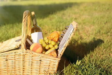 Photo of Picnic basket with snacks and bottle of wine on green grass in park