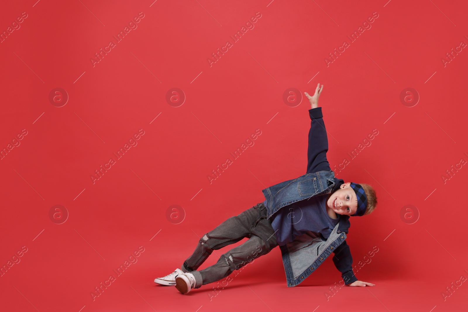 Photo of Happy little boy dancing on red background. Space for text