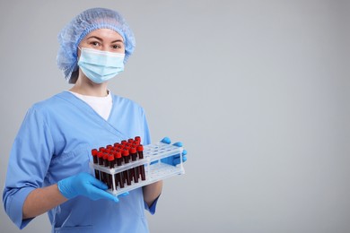 Photo of Laboratory testing. Doctor with blood samples in tubes on light grey background, space for text