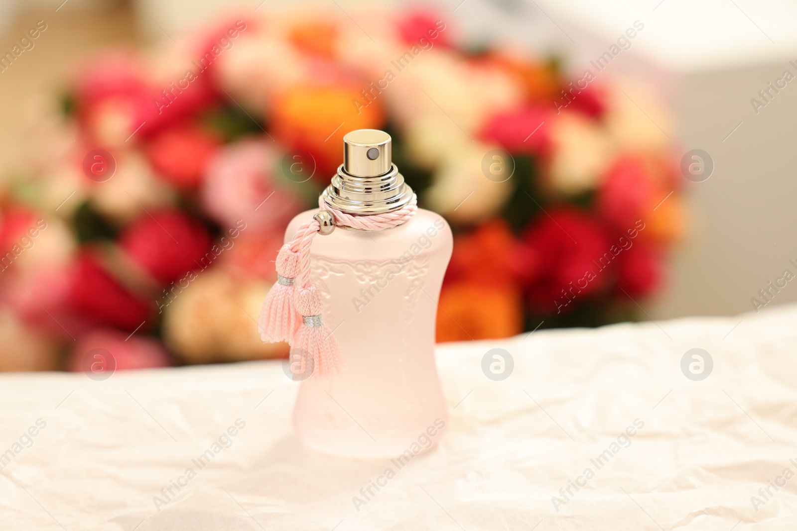 Photo of Bottle of perfume on crumpled paper against beautiful roses, closeup