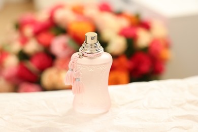 Bottle of perfume on crumpled paper against beautiful roses, closeup