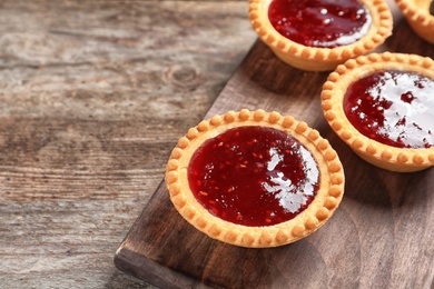 Tasty tartlets with jam on wooden background