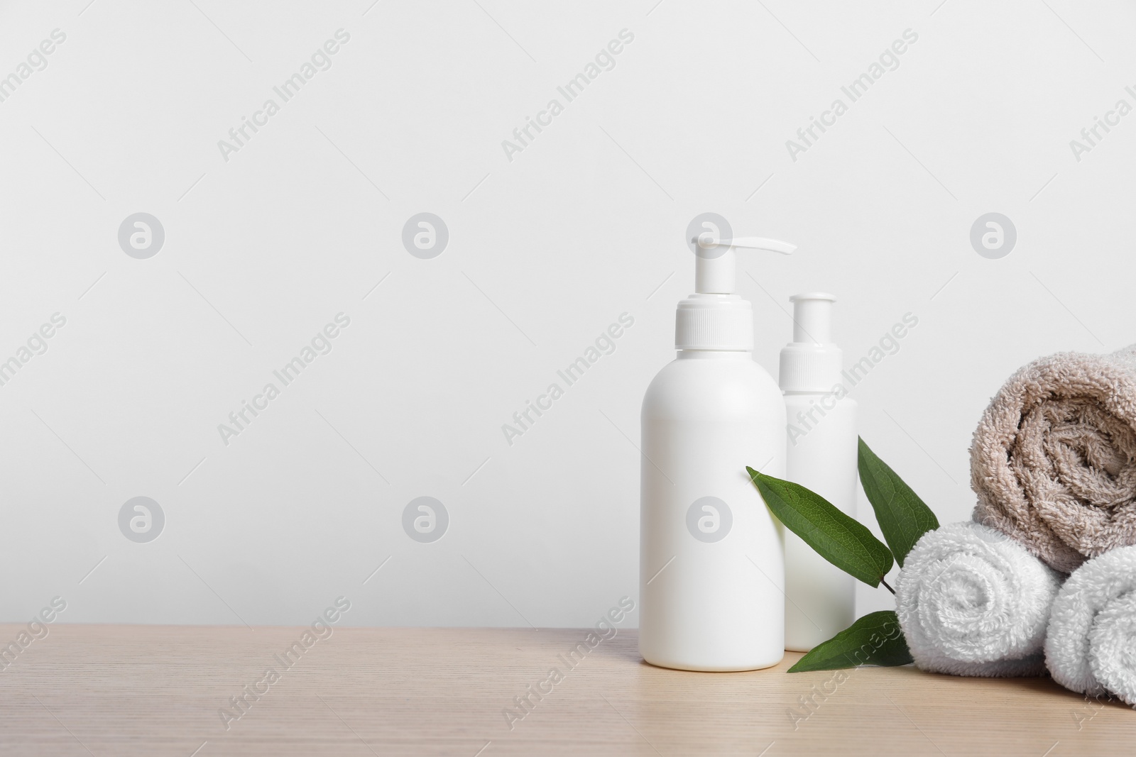 Photo of Bottles of cosmetic products, leaves and towels on wooden table. Space for text