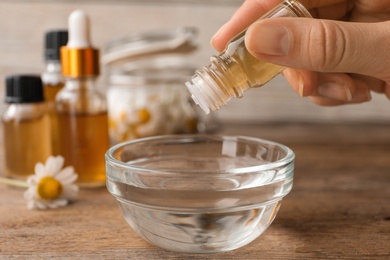 Photo of Woman dripping essential oil into bowl on table, closeup