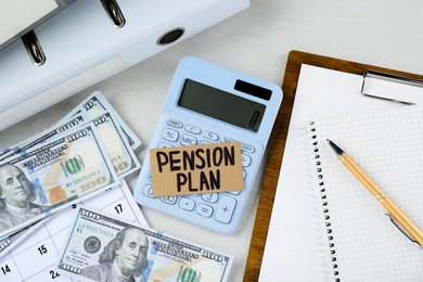 Photo of Card with phrase Pension Plan, dollar banknotes, calculator and notebook on white office table, flat lay