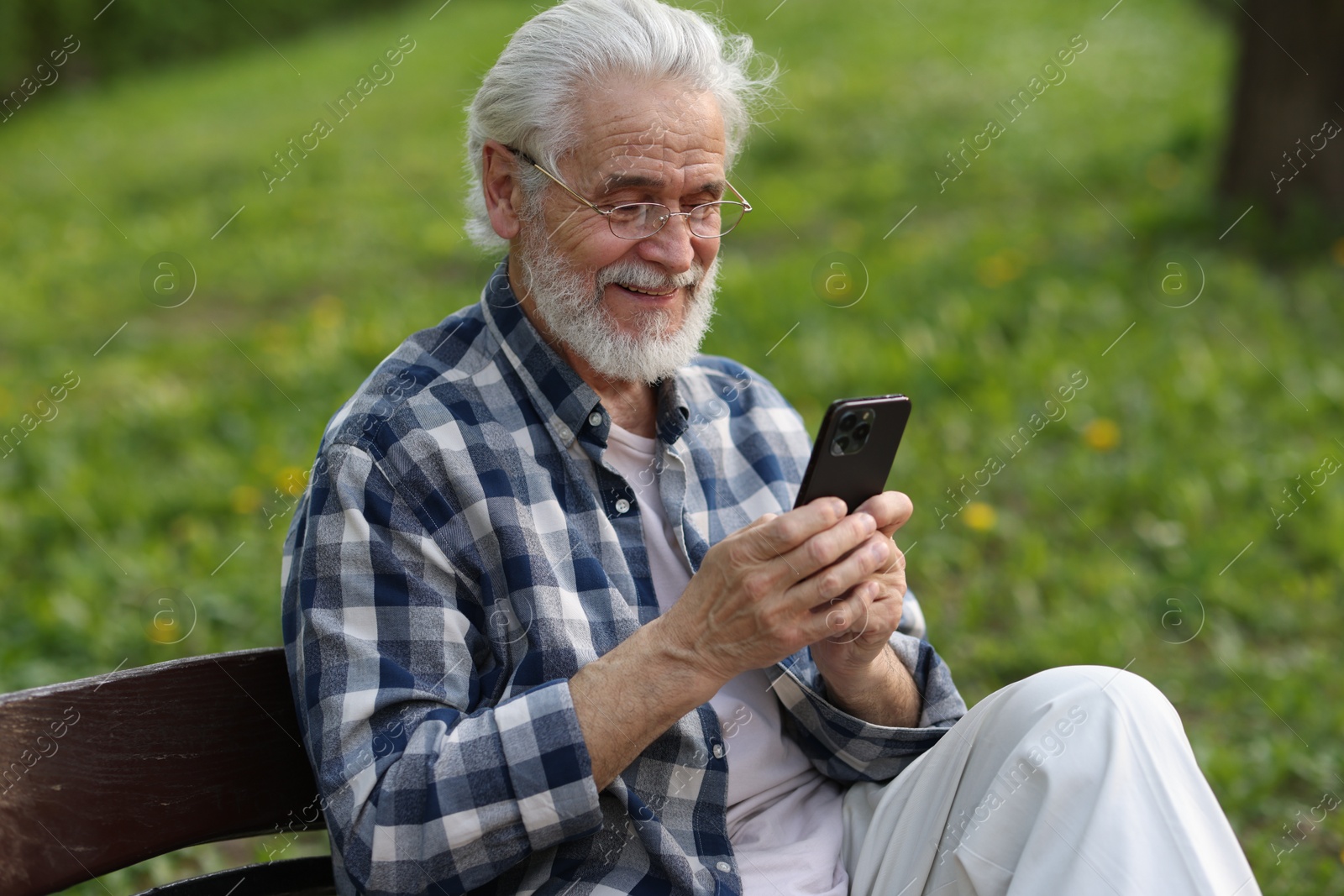 Photo of Portrait of happy grandpa with glasses using smartphone on bench in park