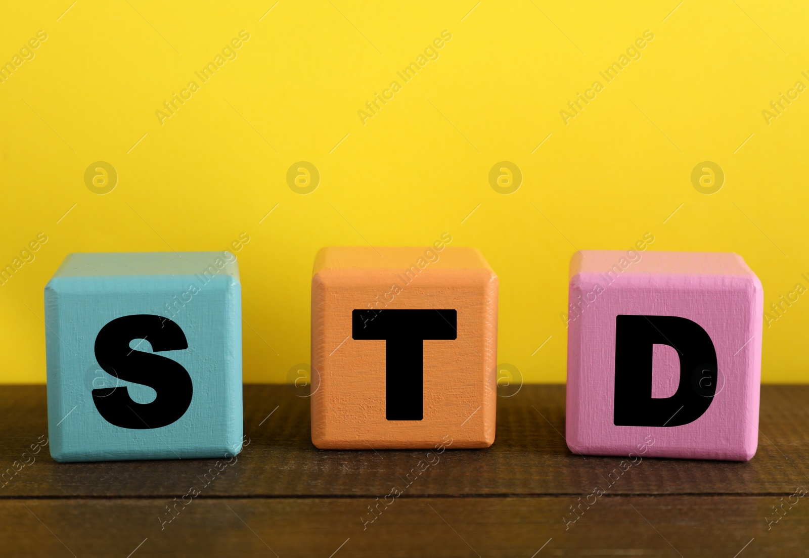 Photo of Abbreviation STD made with cubes on wooden table against yellow background