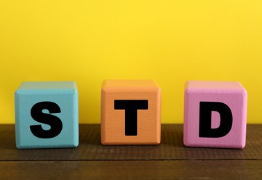 Abbreviation STD made with cubes on wooden table against yellow background