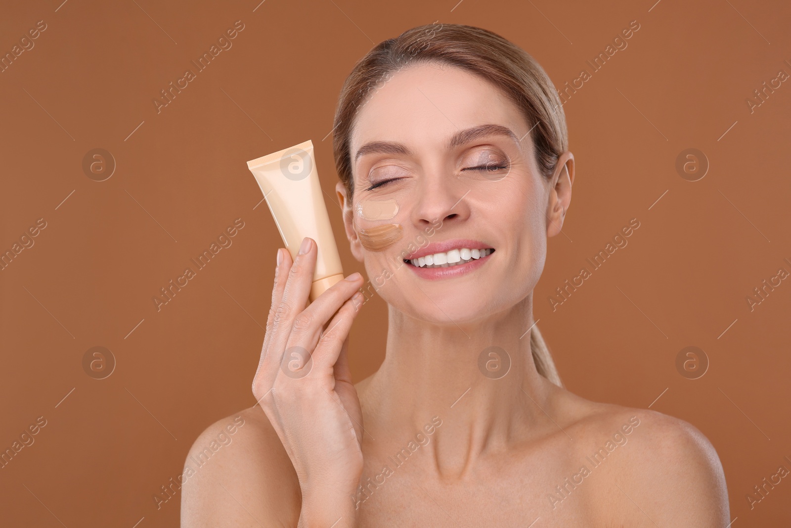 Photo of Woman holding tube of foundation on brown background