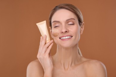 Photo of Woman holding tube of foundation on brown background