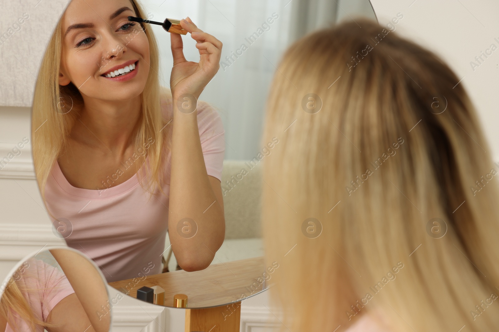 Photo of Beautiful woman applying mascara near mirror at home