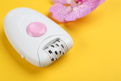 Modern epilator and flower on yellow background