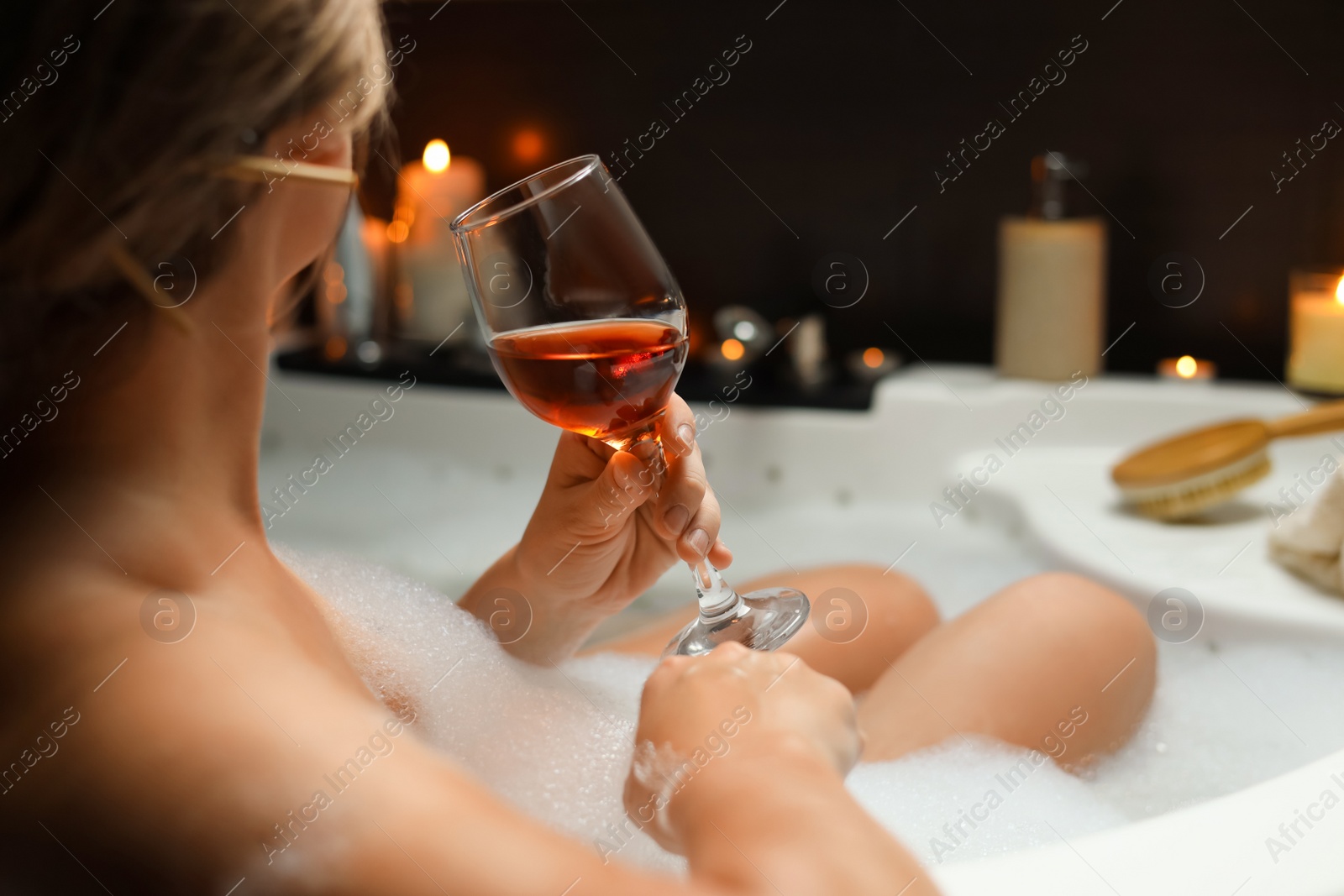 Photo of Woman drinking wine while taking bubble bath, closeup. Romantic atmosphere