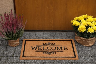 Photo of Doormat with word Welcome and beautiful plants on paving stone near entrance