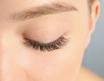 Photo of Young woman with beautiful long eyelashes on gray background, closeup. Extension procedure