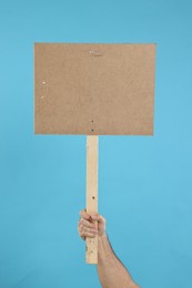 Photo of Man holding blank sign on light blue background, closeup. Space for text