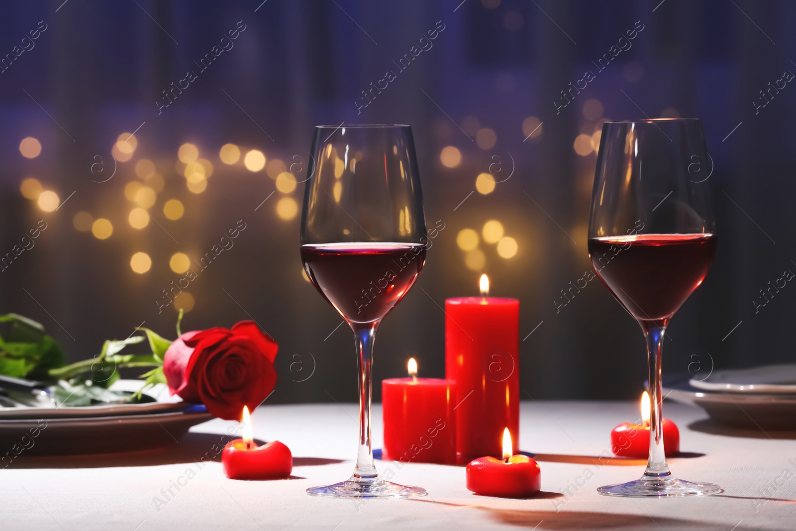 Photo of Beautiful table setting with glasses of wine, candles and rose against blurred lights. Romantic dinner for Valentine's day