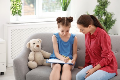 Young female psychologist working with little child in office