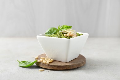 Bowl with delicious pesto sauce, cheese, pine nuts and basil leaves on light table, closeup