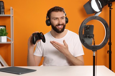 Smiling technology blogger with game controller explaining something while recording video at home