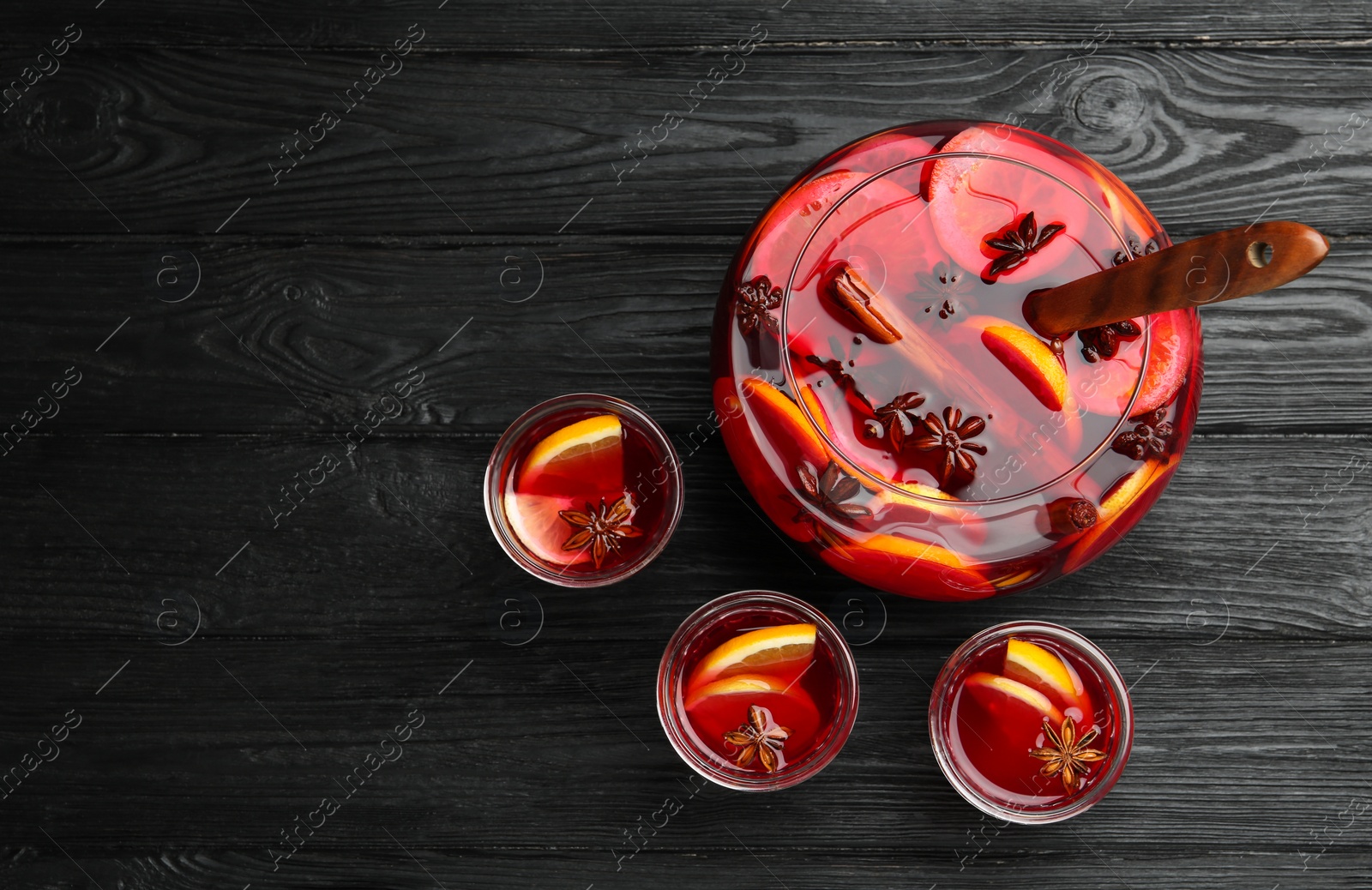 Photo of Glasses near bowl of delicious aromatic punch drink on black wooden table, flat lay. Space for text