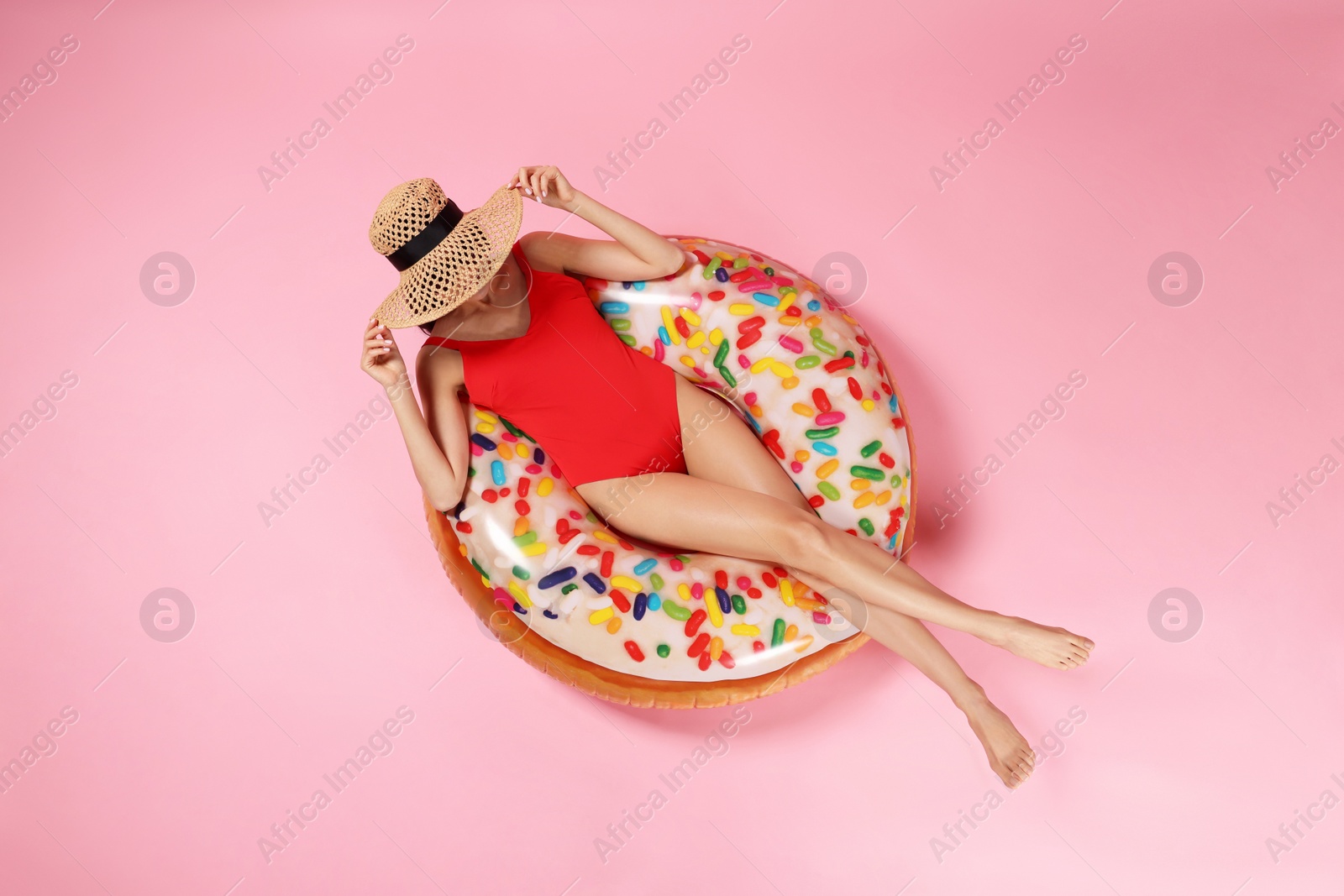 Photo of Young woman in stylish swimsuit on inflatable ring against pink background, top view