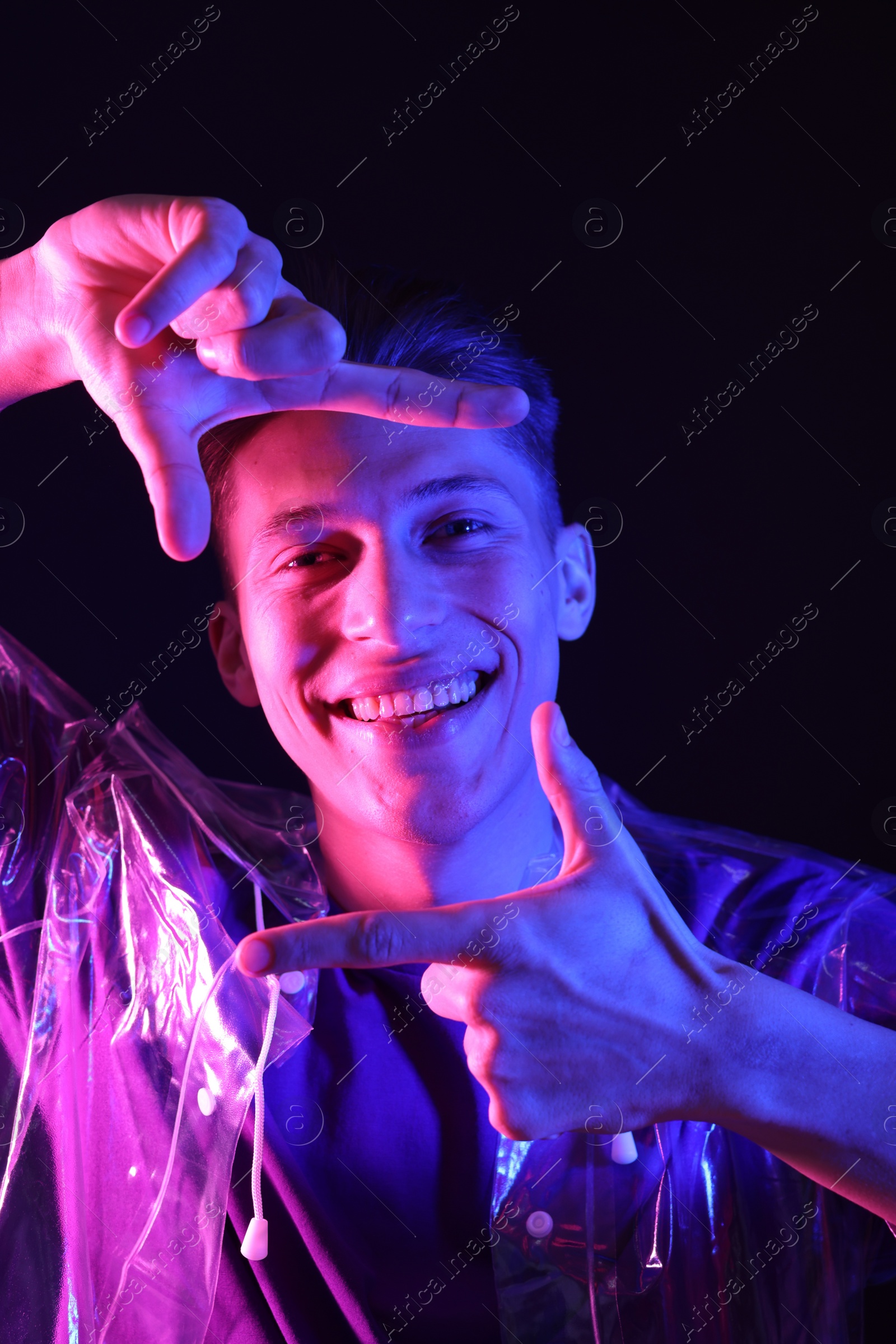 Photo of Young man making camera with hands on dark background in neon lights