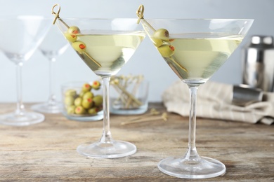 Photo of Glasses of Classic Dry Martini with olives on wooden table against grey background