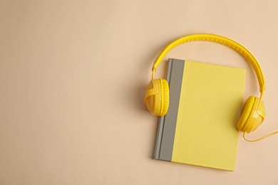 Modern headphones with hardcover book on beige background, top view. Space for text